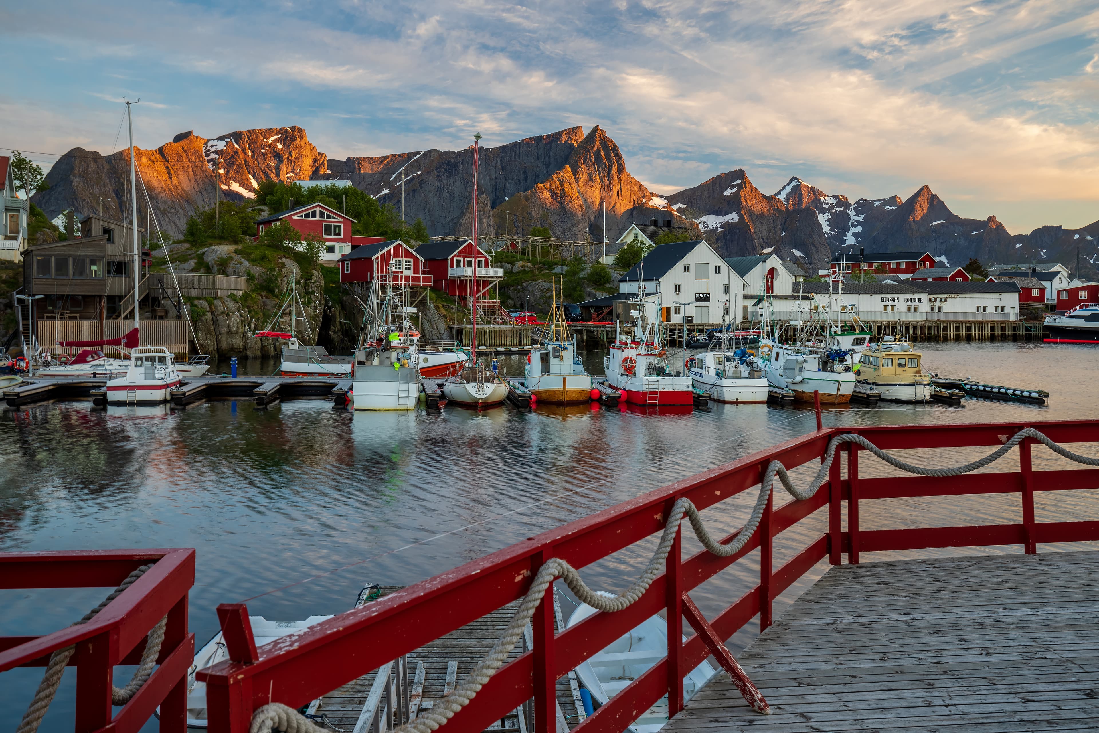 Reine in Lofoten with red fishing cabins, boats and mountains in the background