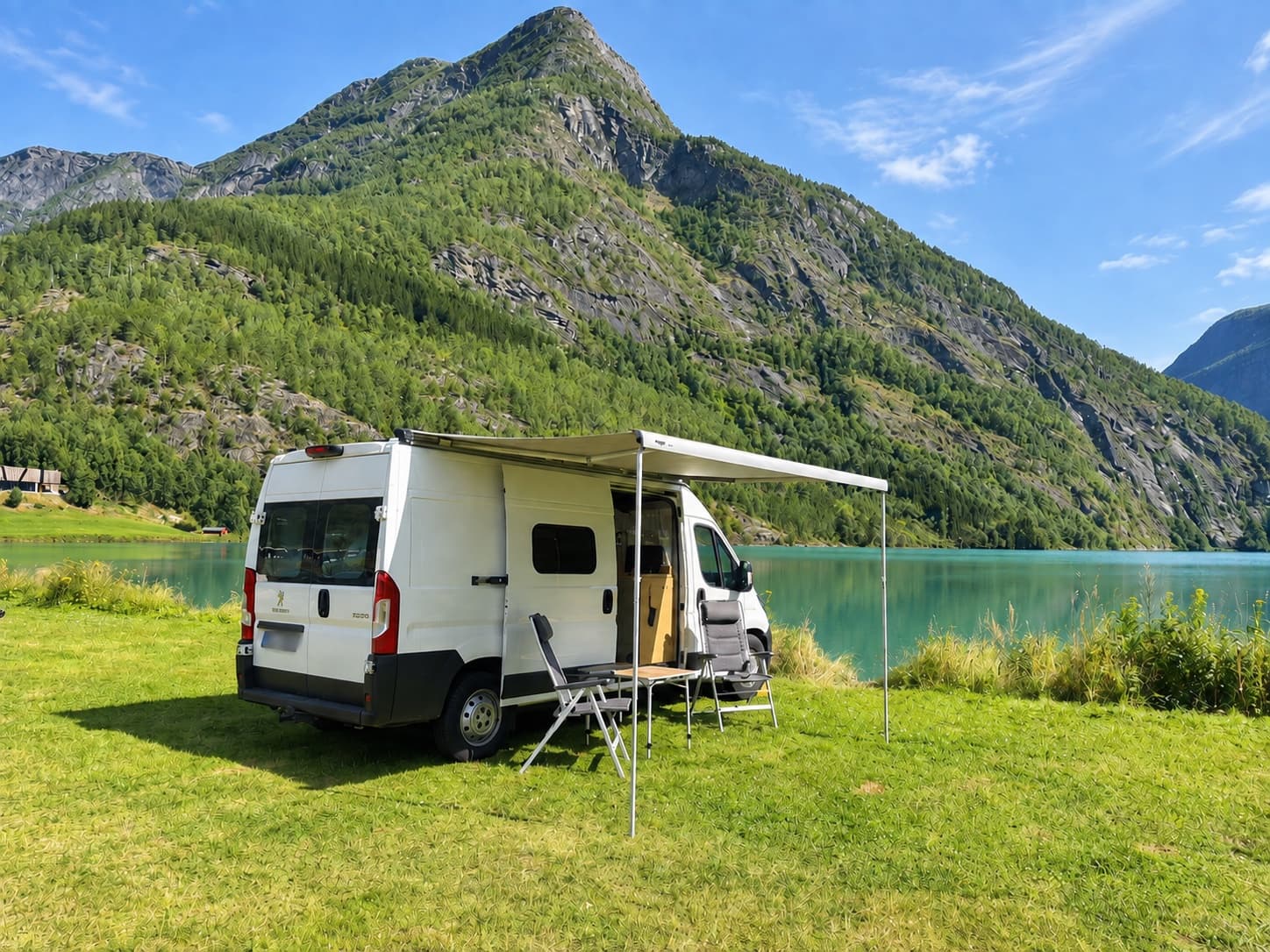 Campervan mit ausgefahrener Markise und Campingstühlen an einem türkisfarbenen Bergsee