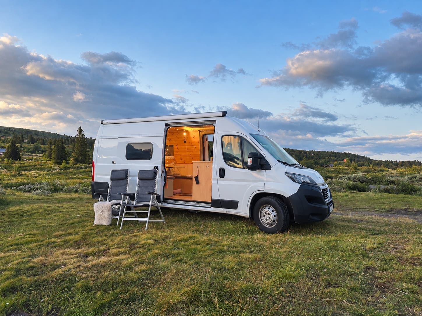 Campervan in der Abenddämmerung in den Bergen mit warmem Licht aus der offenen Schiebetür