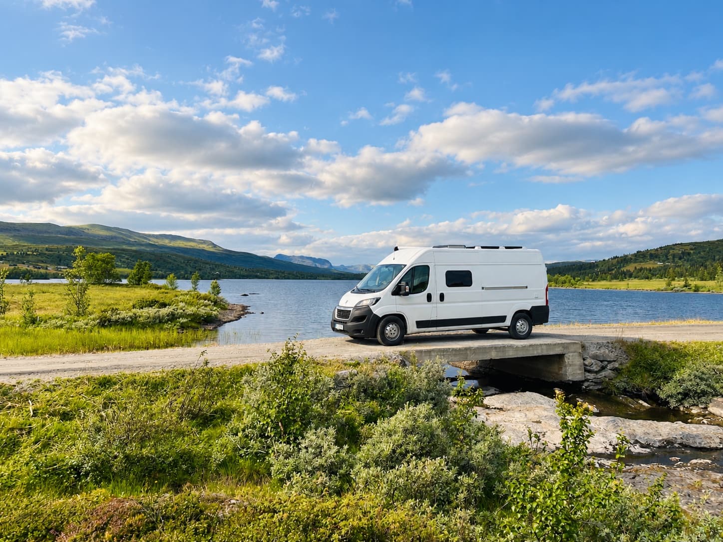 Campervan auf einer kleinen Brücke an einem Bergsee unter blauem Himmel