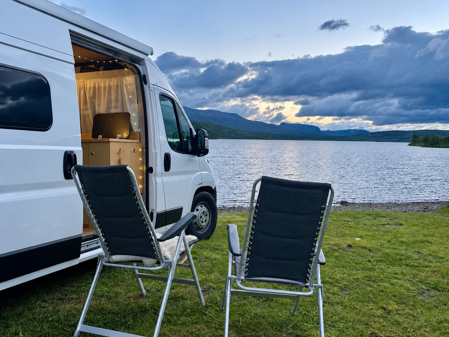 Campingstühle neben dem Campervan mit Blick auf einen Bergsee in der Abenddämmerung
