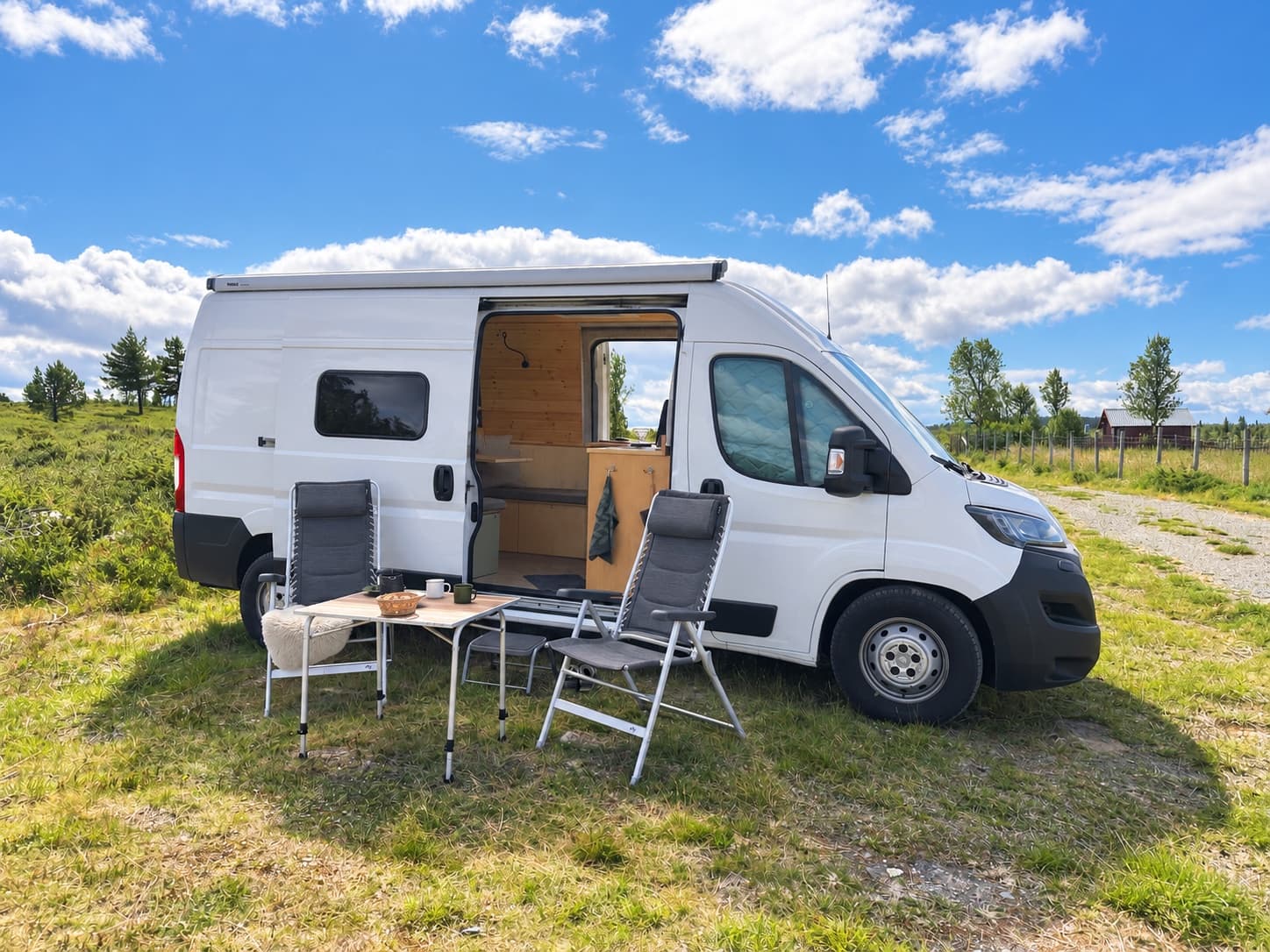 Campervan mit Campingtisch und Stühlen unter blauem Himmel